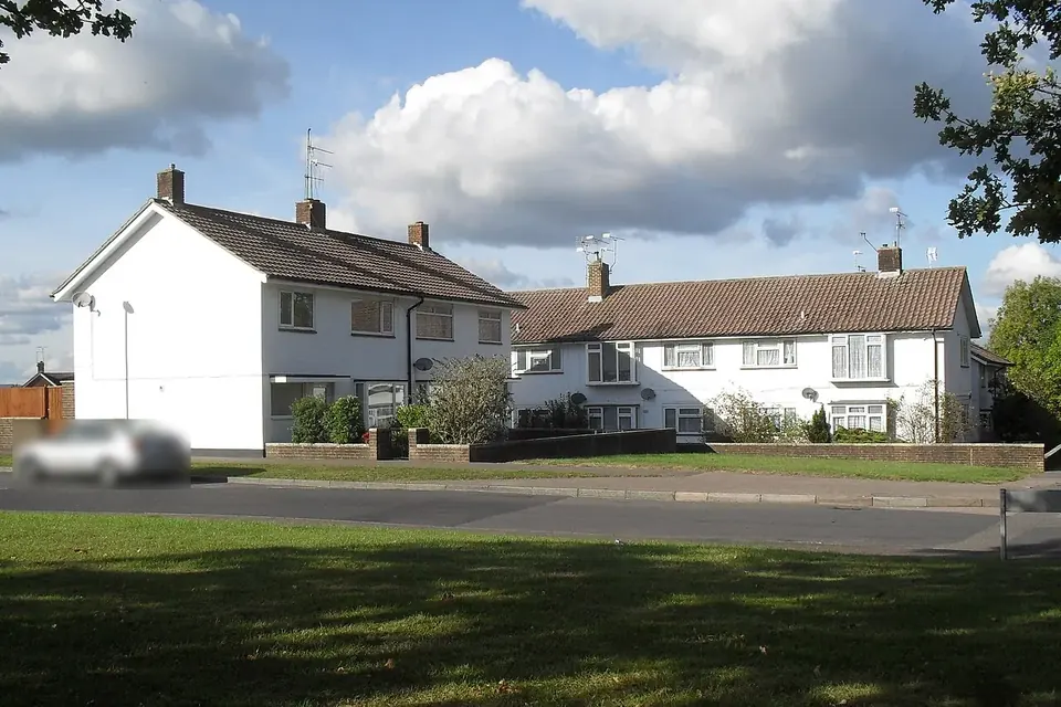 A short row of white-rendered terraced houses with tiled roofs behind a strip of lawn on a sunny day