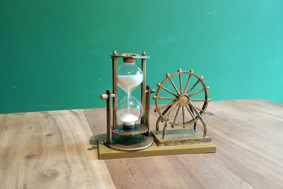 A small brass hourglass with sand gathering in the lower bulb, on a wooden table