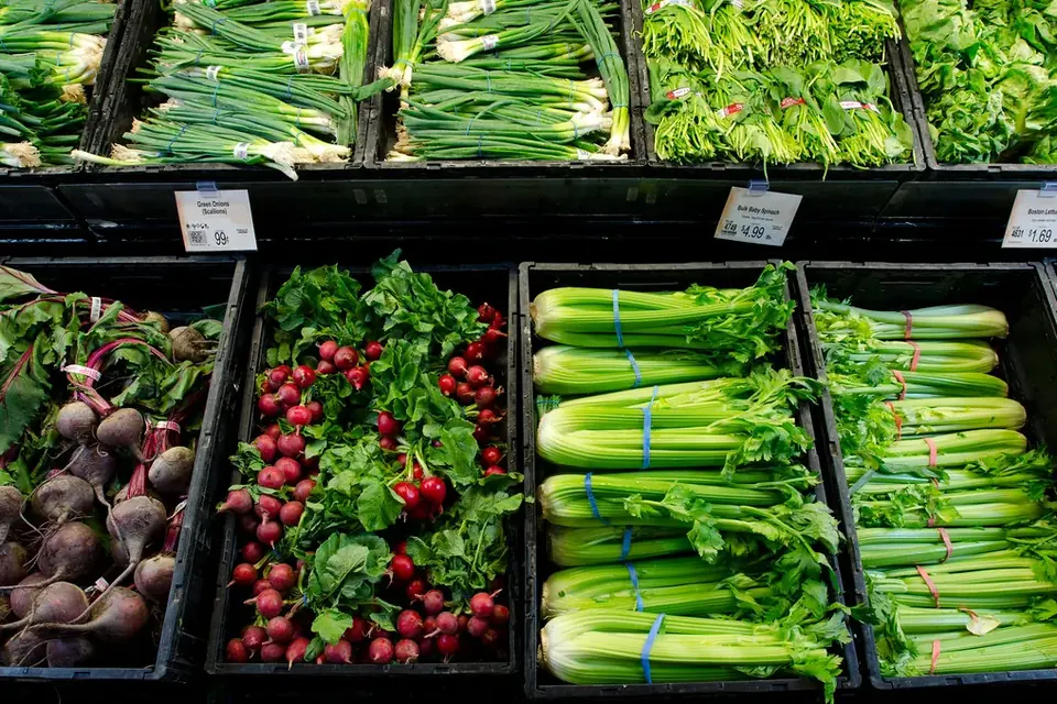 Bins of radishes, beetroot, celery and spring onions arranged side by side on a shop shelf
