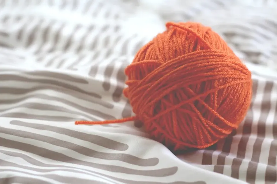 A ball of orange wool with a loose strand on a striped blanket