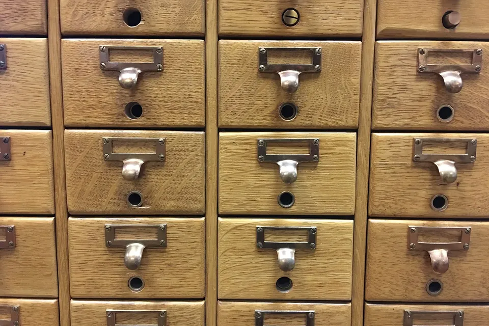 Rows of small wooden drawers with brass handles and label holders in a card catalogue